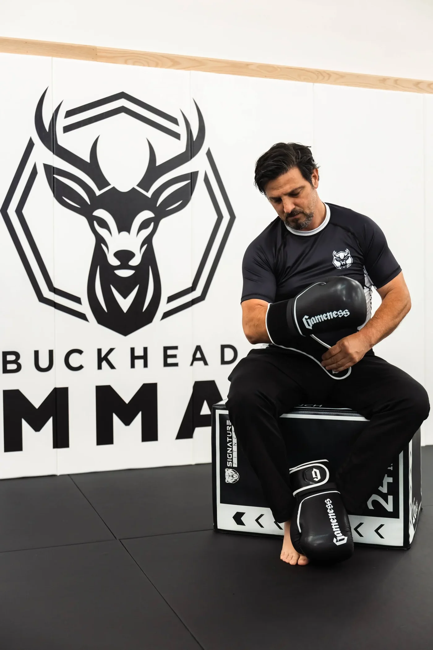 A coach laces gloves under the Buckhead MMA deer on the gym wall.